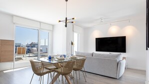 Una sala de estar moderna con una mesa de comedor de vidrio, sillas de mimbre, un sofá gris y un televisor de pantalla plana grande.