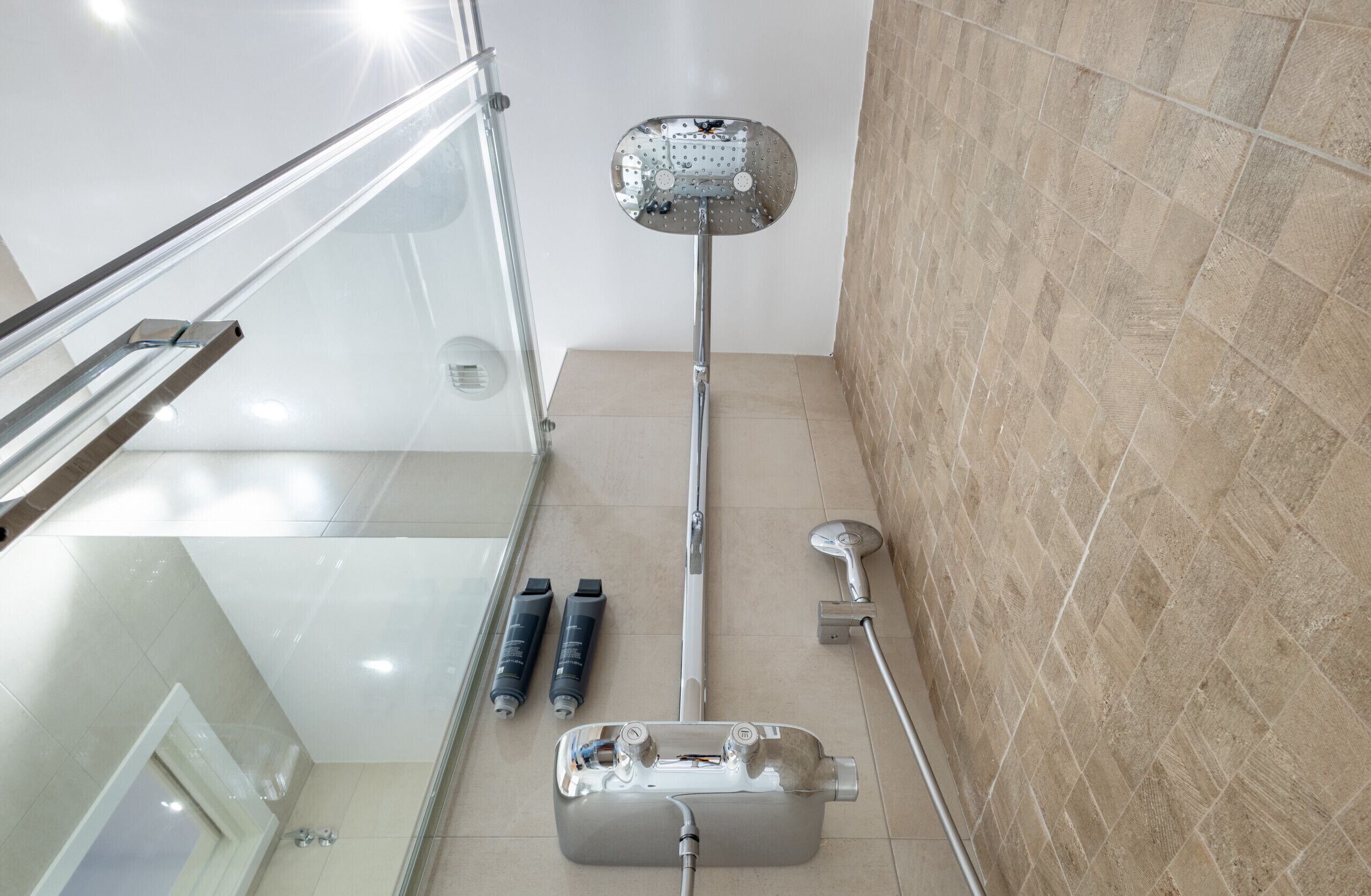 A modern bathroom with a glass shower enclosure, a handheld showerhead, a handheld showerhead, and a wall-mounted faucet.