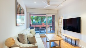 Un salon moderne avec un canapé, une table basse en bois, un téléviseur et un balcon équipé d’une table et de chaises.