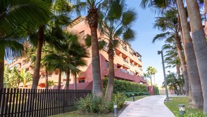 Un immeuble à plusieurs étages doté de balcons, entouré de palmiers et bordé d’une promenade dallée.