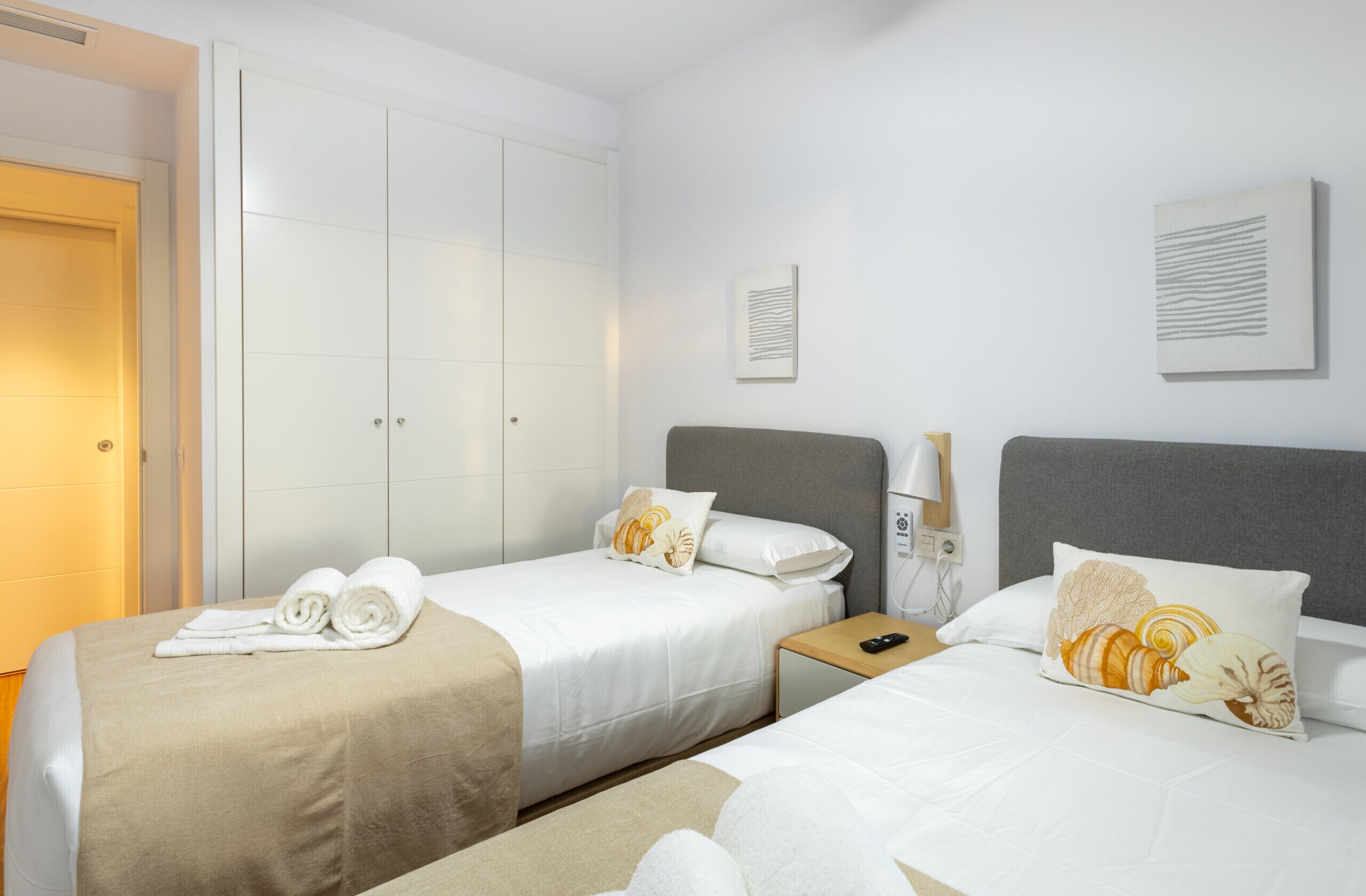 Habitación de hotel con dos camas, un armario, una mesita de noche con lámpara y una obra de arte en la pared.