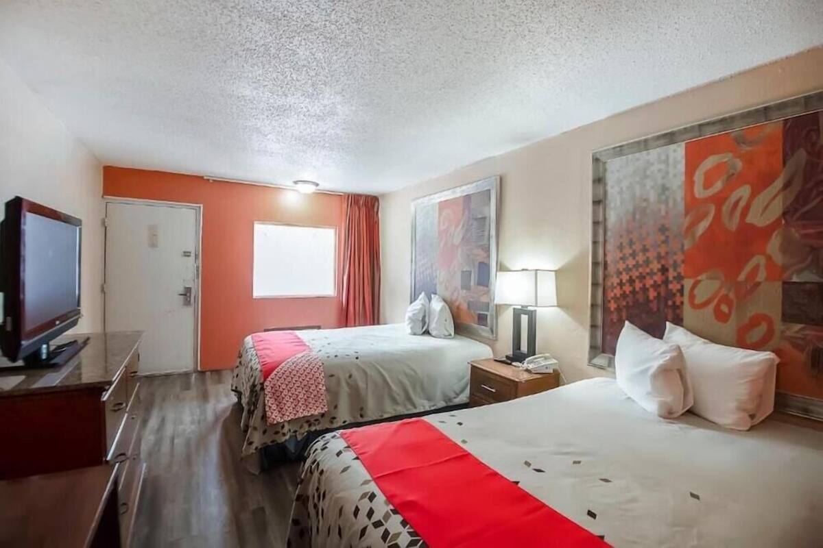 A hotel room with two beds, a television, a desk, and a window with curtains.