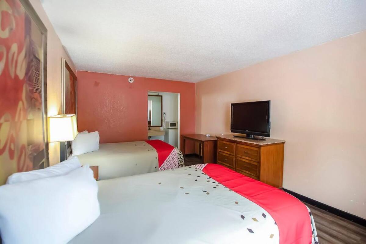 A hotel room with two beds, a television, a desk, and a mirror.
