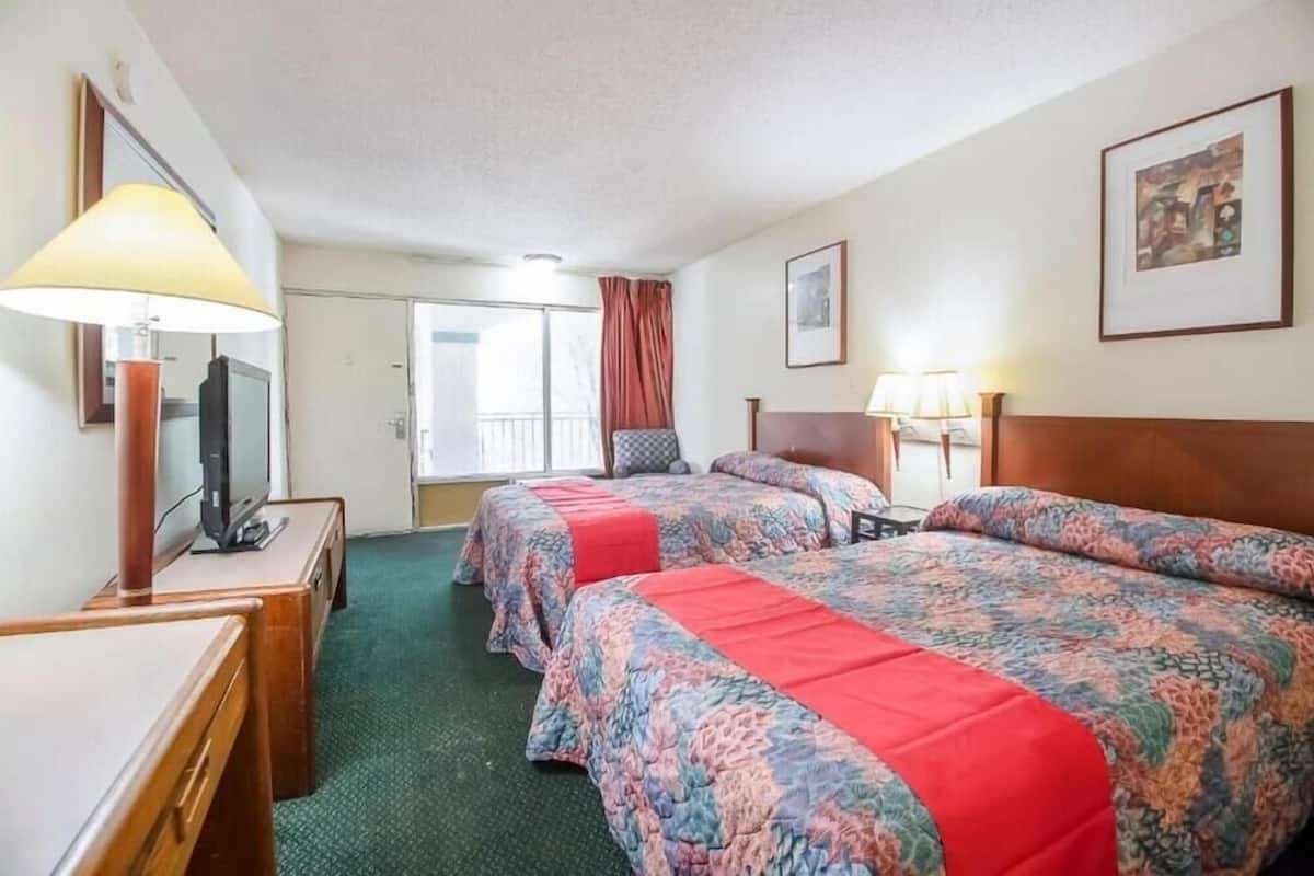 A hotel room with two beds, a television, a desk, and a window with curtains.