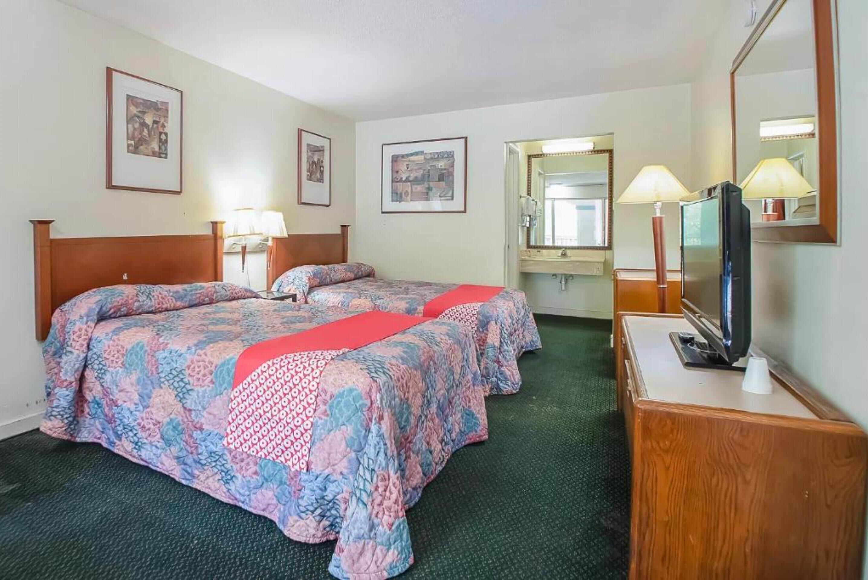 Een hotelkamer met twee bedden, een bureau met een televisie, en ingelijste foto’s aan de muur.
