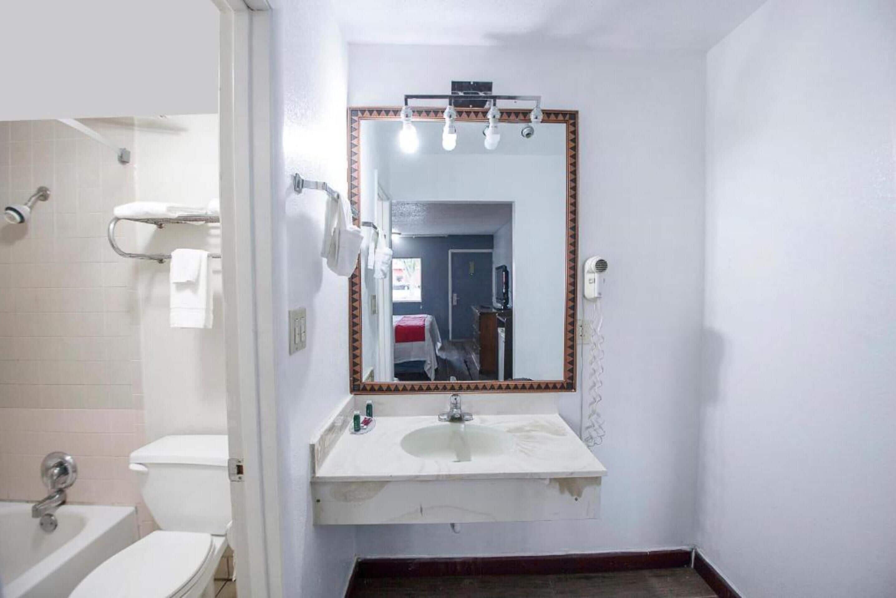A bathroom with a white sink, a mirror with lights, a toilet, and a shower.