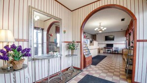 A room with striped wallpaper, a mirror, a small table with a lamp, a vase with flowers, and a checkered floor. - Hotel O Daylight Inn Elkhart I-90, In (Elkhart)