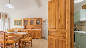 Een houten eettafel met stoelen, een kast met glazen deuren, en een keuken met groene kasten.
