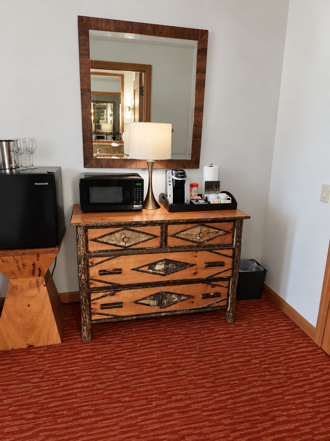 Habitación de hotel con una mesita de madera, microondas, cafetera y televisión.