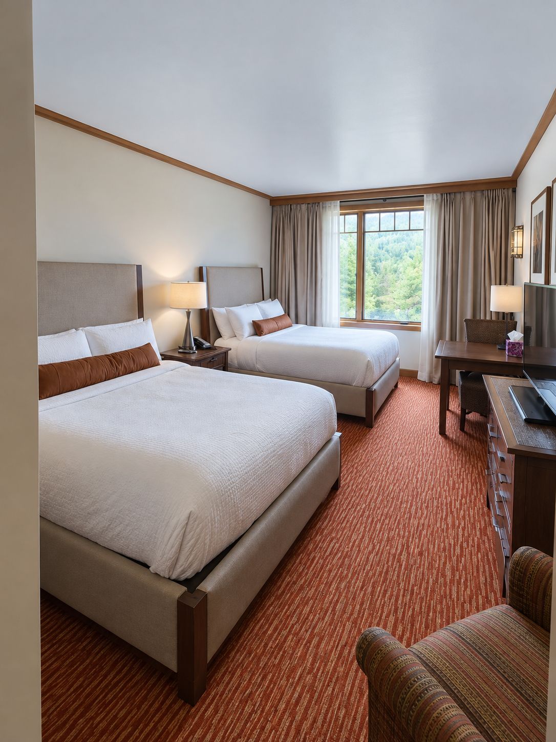 Une chambre d’hôtel avec deux lits, un bureau, une chaise et une fenêtre avec des rideaux.
