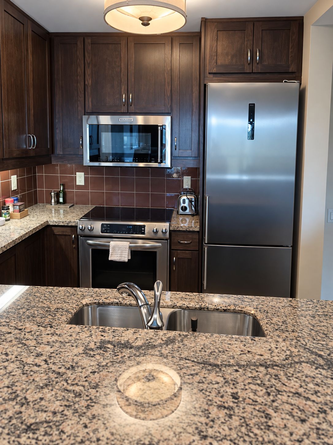Una cocina con armarios de madera oscura, un refrigerador de acero inoxidable, un microondas y una encimera de granito.
