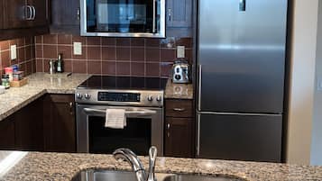 Una cocina con armarios de madera oscura, un refrigerador de acero inoxidable, un microondas y una encimera de granito.