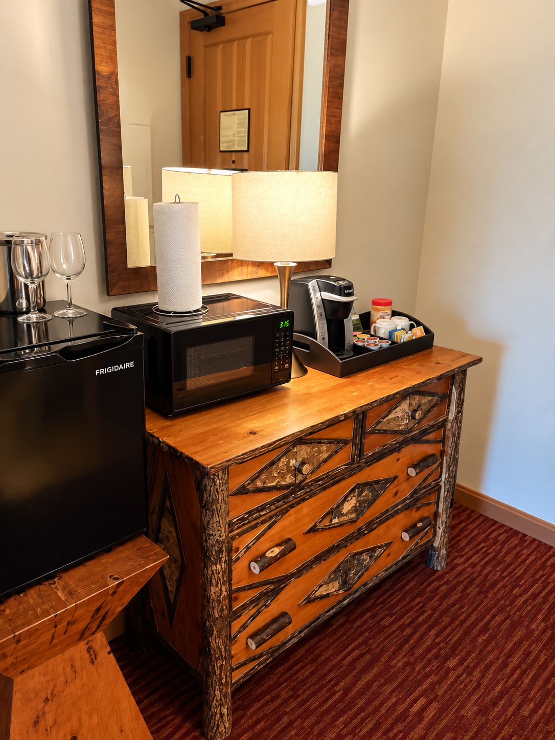 Habitación de hotel con minibar, microondas, cafetera y un mueble de madera decorativo.