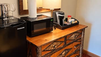 Habitación de hotel con minibar, microondas, cafetera y un mueble de madera decorativo.
