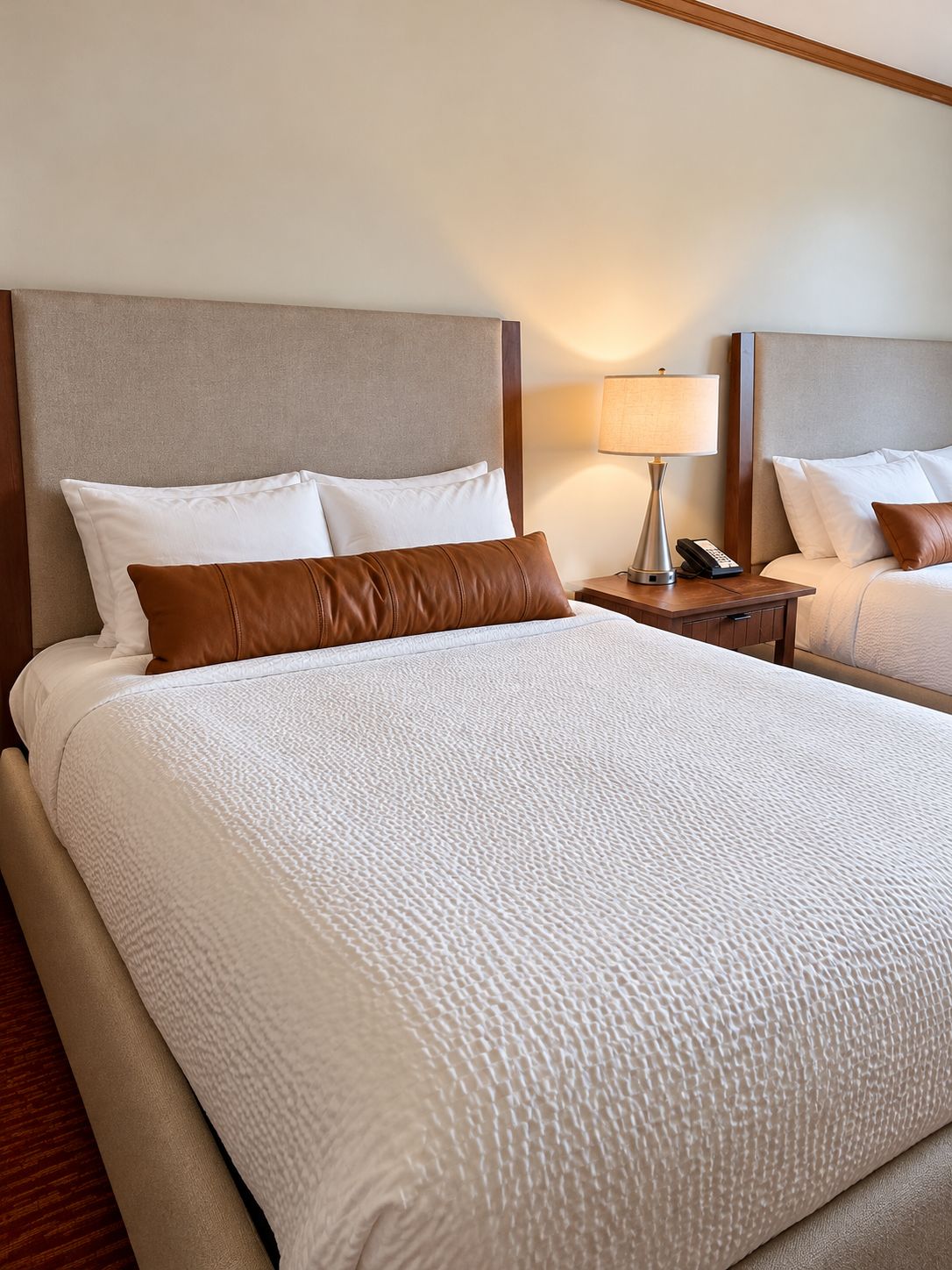 Habitación de hotel con una cama grande, dos almohadas, una mesita de noche con lámpara y un teléfono.