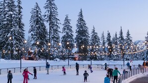 Un espace extérieur enneigé où l’on peut faire du ski et du snowboard, entouré d’arbres couverts de neige et illuminé par des guirlandes lumineuses.