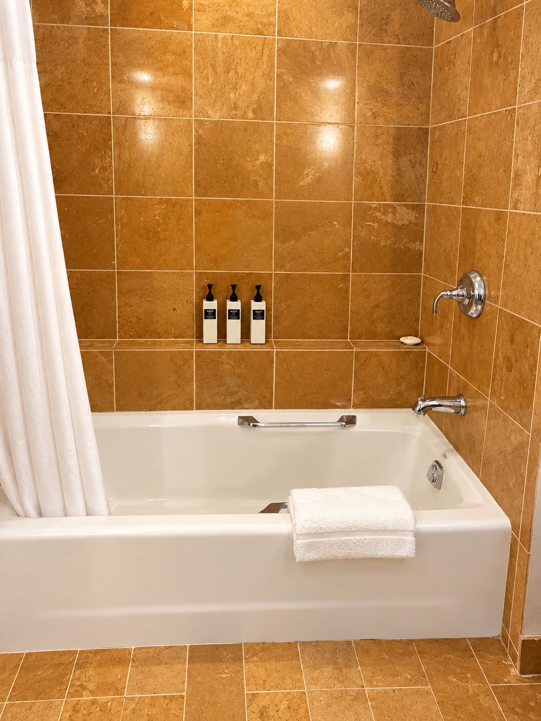 Un baño con una bañera blanca, un cabezal de ducha y tres botellas de artículos de aseo en la pared.