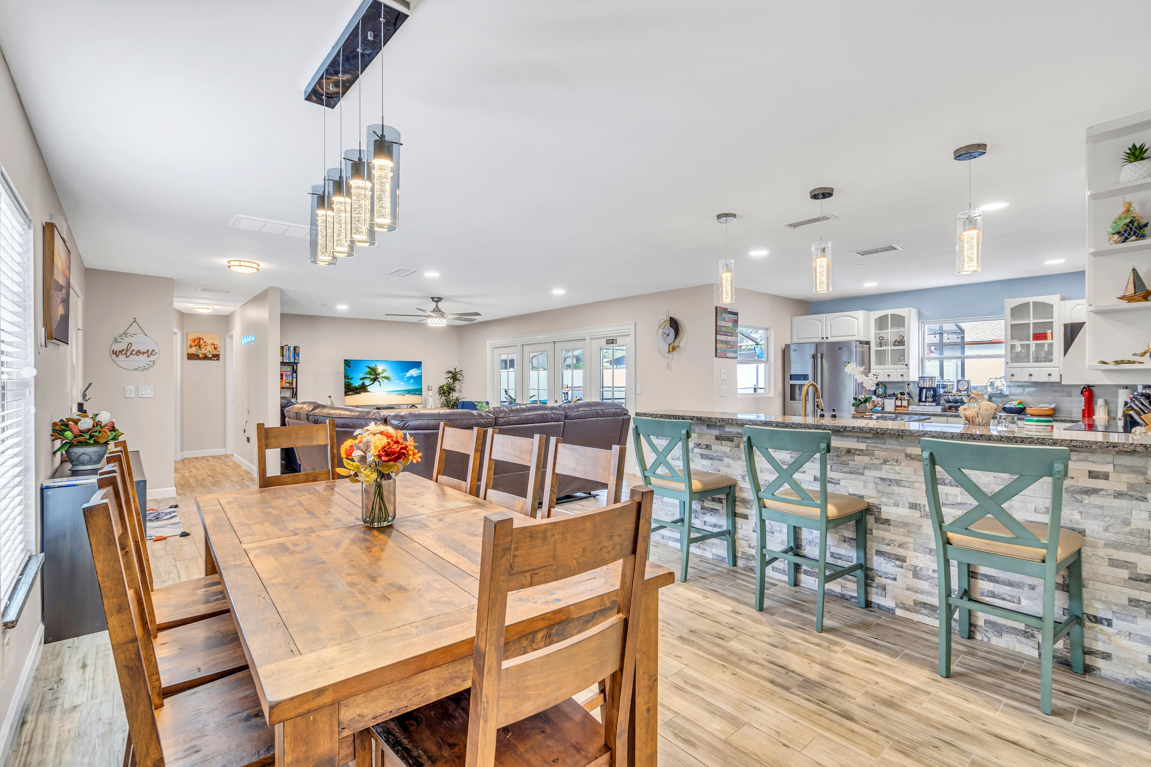A spacious kitchen with a central island, wooden dining table, and modern pendant lighting.