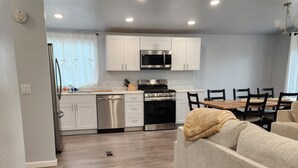 A modern kitchen with white cabinets, a stainless steel stove, and a microwave. There is a dining area with a wooden table and chairs. - Red Mesa house  (Page)