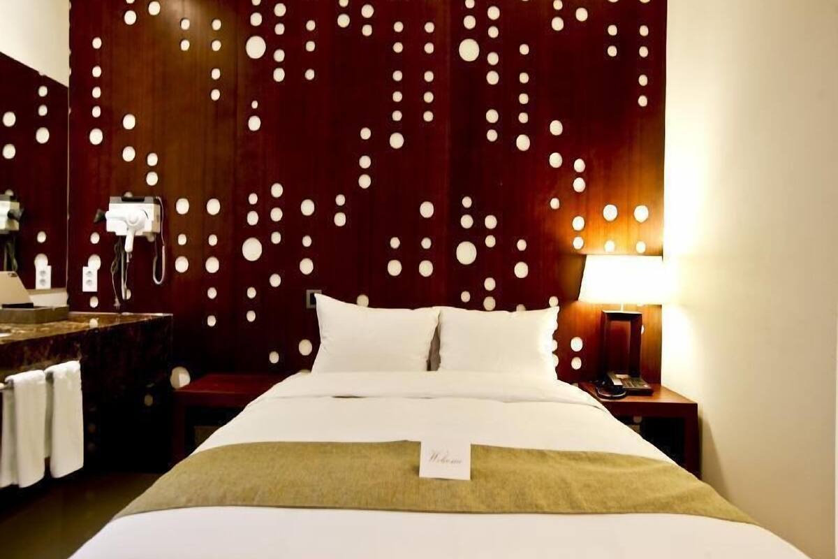 Ein Hotelzimmer mit Bett, Nachttisch, Lampe, Spiegel und einer Wand mit kreisförmigem Muster.
