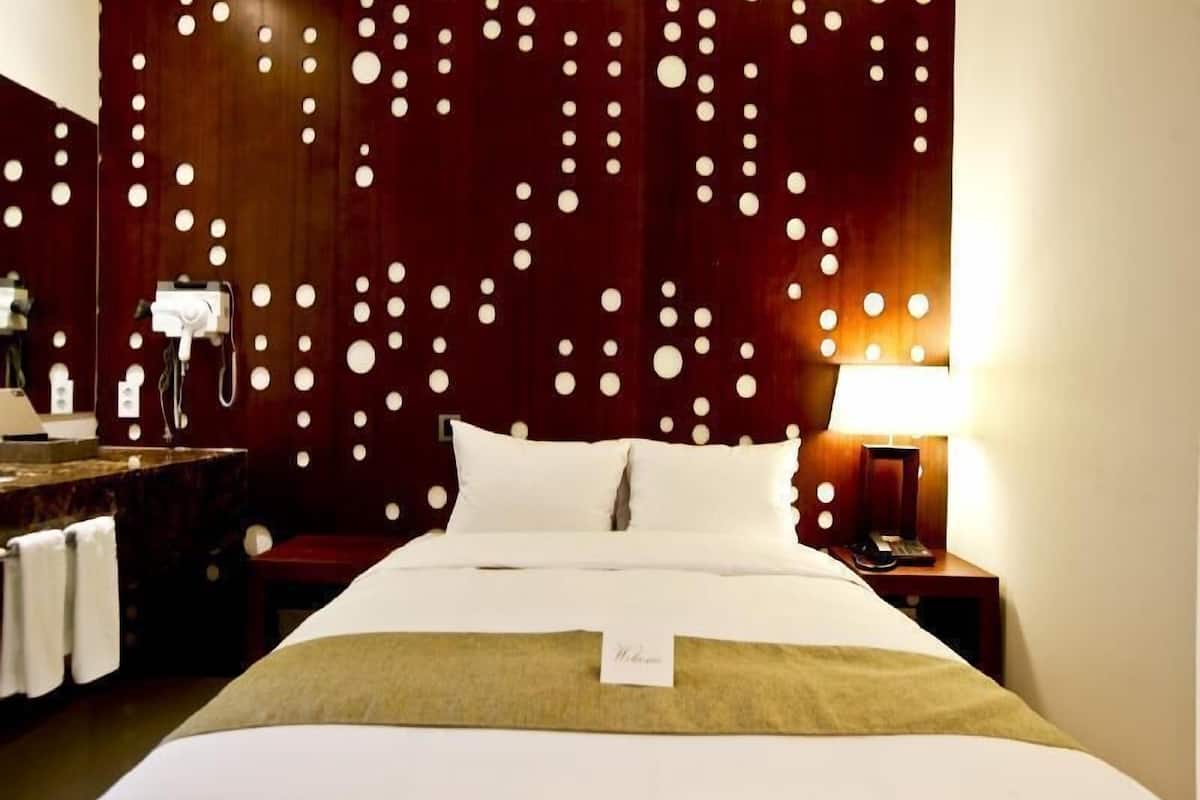 A hotel room with a bed, a nightstand, a lamp, a mirror, and a wall with circular patterns.