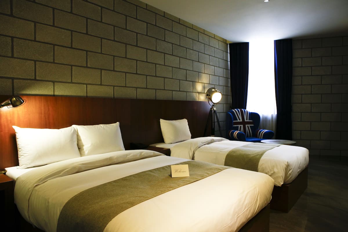 Ein Hotelzimmer mit zwei Betten, einer Ziegelwand, einem Schild mit der Aufschrift "Welcome" und einem Sessel mit Union-Jack-Flagge.