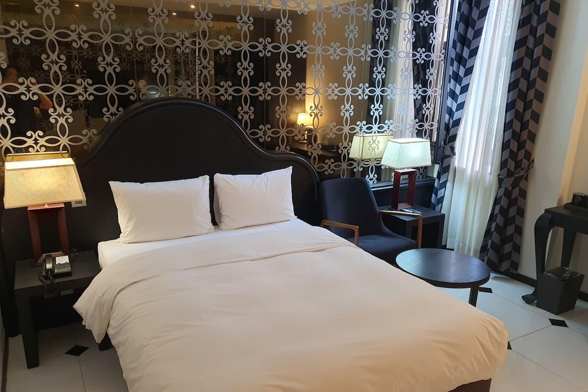Ein Hotelzimmer mit einem großen Bett, zwei Nachttischen, einem Sessel, einem kleinen Tisch und dekorativen Vorhängen.
