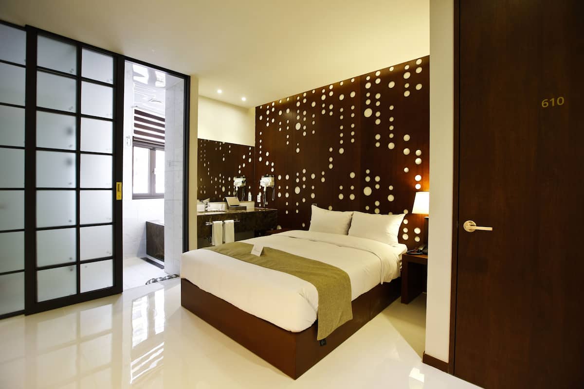 Ein modernes Hotelzimmer mit einem großen Bett, einem hölzernen Kopfteil mit kreisförmigen Mustern, einem separaten Badezimmer mit Schiebetür und der sichtbaren Zimmernummer 610.