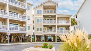 A multi-story building with balconies, a covered parking area, and a clear sky.