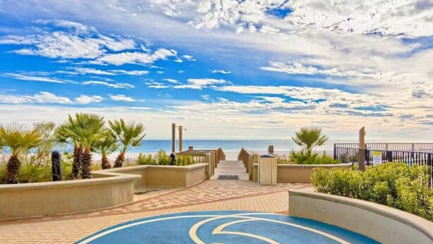 A pathway leading to a beach with palm trees and a clear sky.