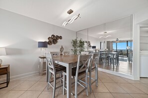 A modern dining area with a wooden table and chairs, a large mirror reflecting the room, and a view of the outdoor patio.