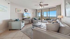 A modern living room with a sofa, armchair, and coffee table. There is a television and artwork on the wall.