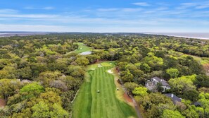 An aerial view of a golf course with a clubhouse, surrounded by dense trees and a distant shoreline. - Contemporary Seascape Villa, Popular Kiawah West Beach, 1BR, Steps to Beach! (Kiawah Island)
