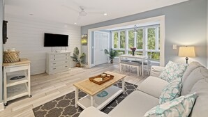 A modern living room with a flat-screen TV, a wooden coffee table, a sofa with starfish-patterned pillows, and a dining area with a table and chairs. - Contemporary Seascape Villa, Popular Kiawah West Beach, 1BR, Steps to Beach! (Kiawah Island)