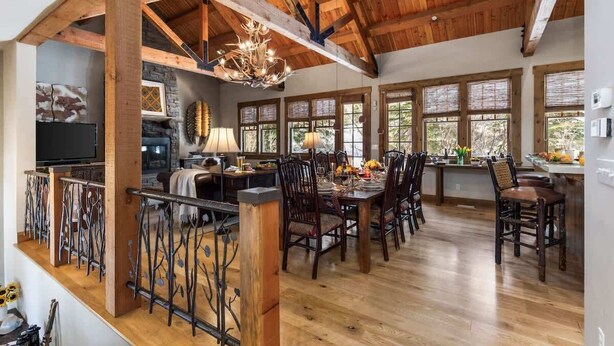 A spacious dining area with a high ceiling and wooden beams, large windows, and a fireplace. - Abode at Granite Ridge, luxury lodge, sound system (Teton Village)