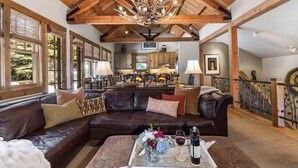 A spacious living area with a leather sofa, a coffee table with flowers and wine, and a kitchen in the background. - Abode at Granite Ridge, luxury lodge, sound system (Teton Village)