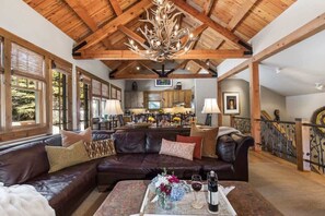 A spacious living area with a leather sofa, a coffee table with flowers and wine, and a kitchen in the background.
