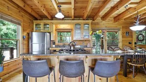 Interior de una cabaña de madera con cocina, taburetes de bar y comedor.