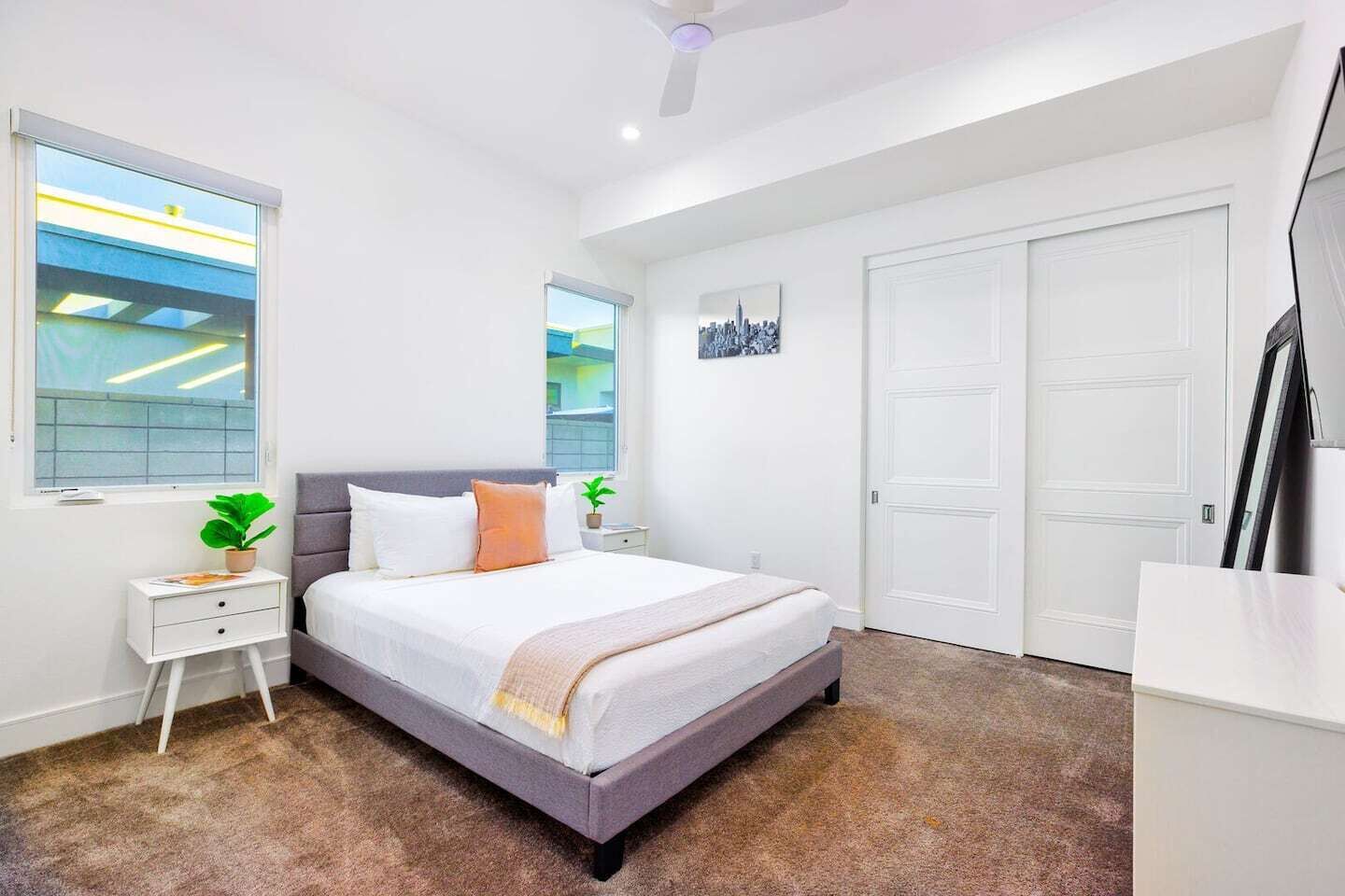 Une chambre à coucher avec un lit, une table de chevet, une plante en pot, une fenêtre et une porte.