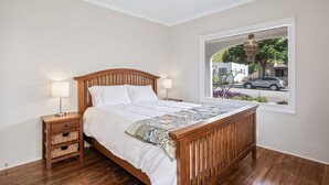 A bedroom with a wooden bed, two bedside tables, a window with a view of the street, and a ceiling fan. - Amazing Reviews, Great Location (Ventura)