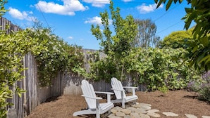 A backyard with a wooden fence, two white Adirondack chairs, and a stone pathway. - Amazing Reviews, Great Location (Ventura)