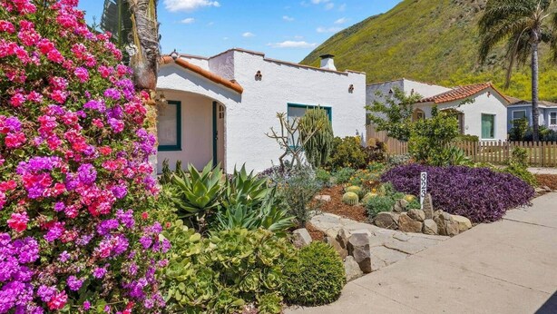 A white building with a green door and windows, surrounded by colorful flowers and plants. - Amazing Reviews, Great Location (Ventura)