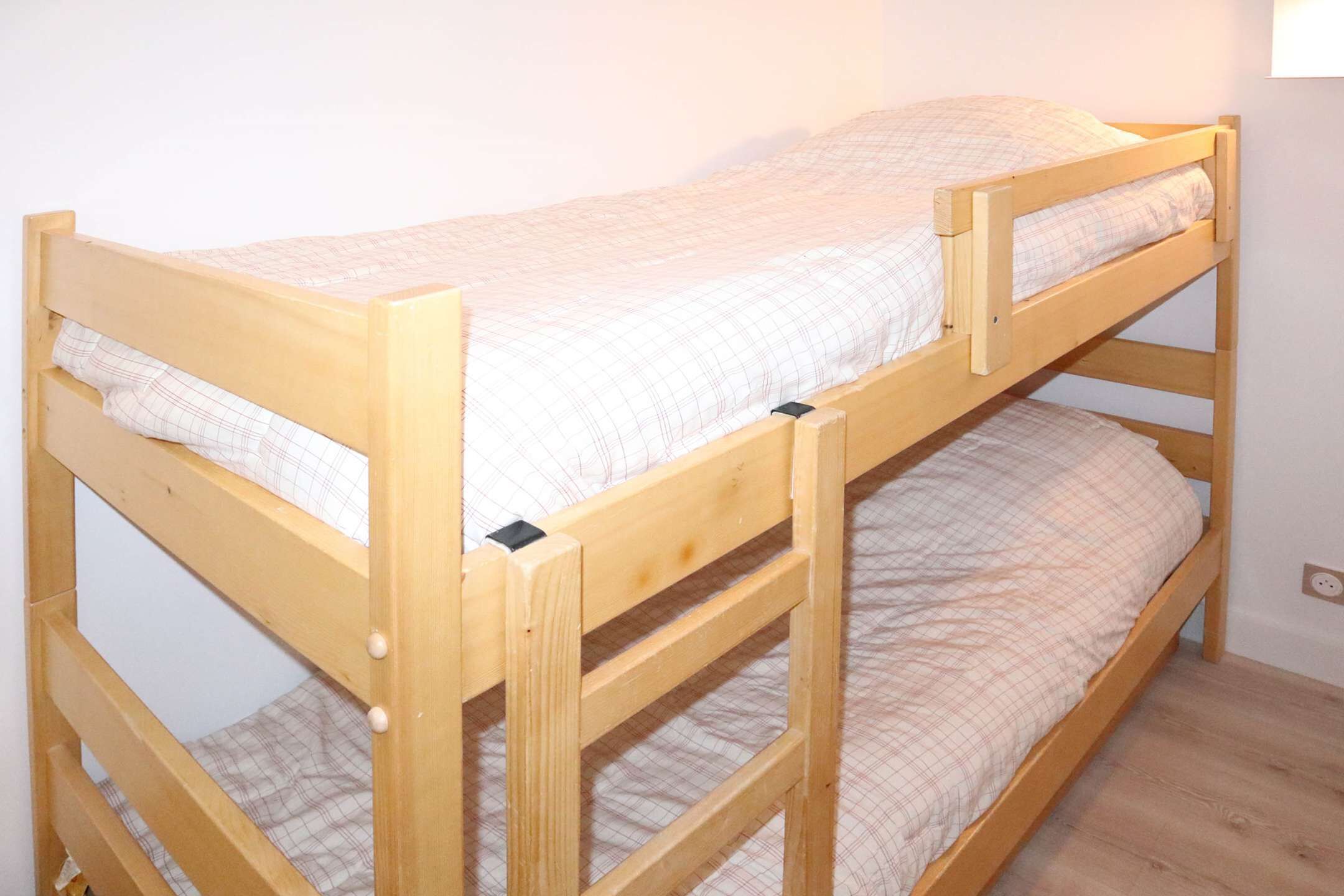 A bunk bed with a wooden frame and a plaid bedspread.