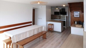 A small, cozy room with a single bed, a wooden bench, a small stool, and a kitchenette area.