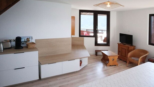 A modern bedroom with a bed, a TV, a wooden cabinet, a wicker chair, and a small table.