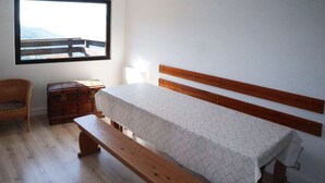 A bedroom with a wooden bed, a bench, a wicker chair, and a chest of drawers.