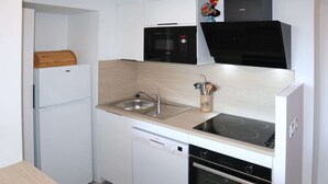 A compact kitchen with a dishwasher, stove, microwave, and a small refrigerator.
