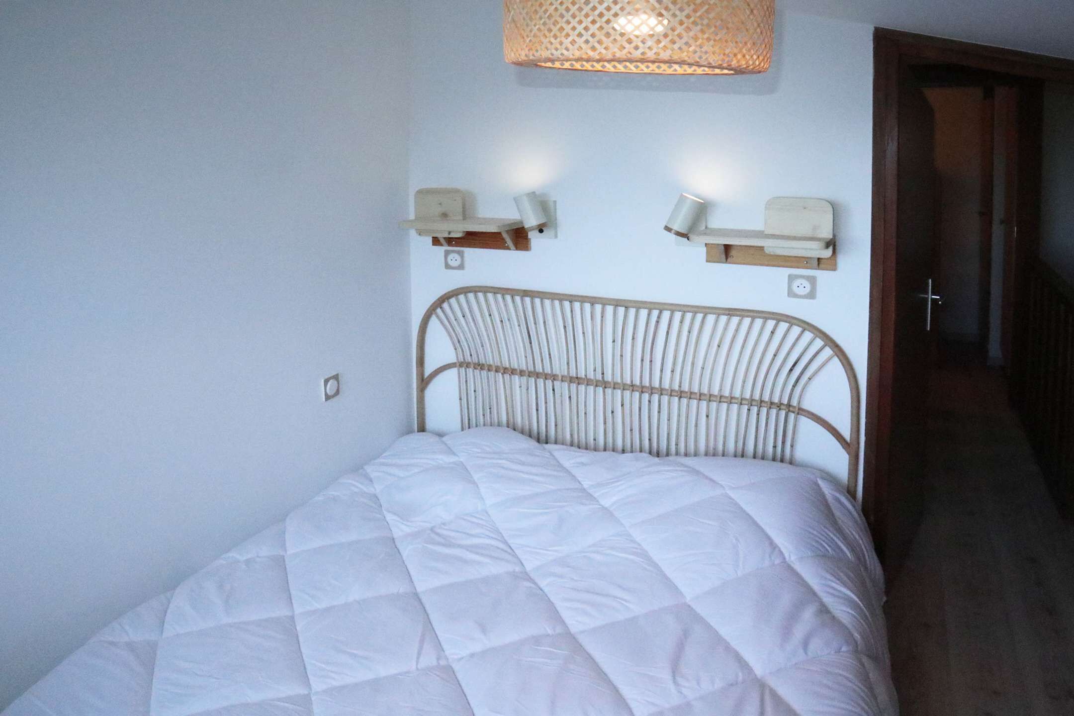 Een bed met een wit geborduurde matras, een metalen hoofdbord en twee nachtkastjes aan de muur met lampen.