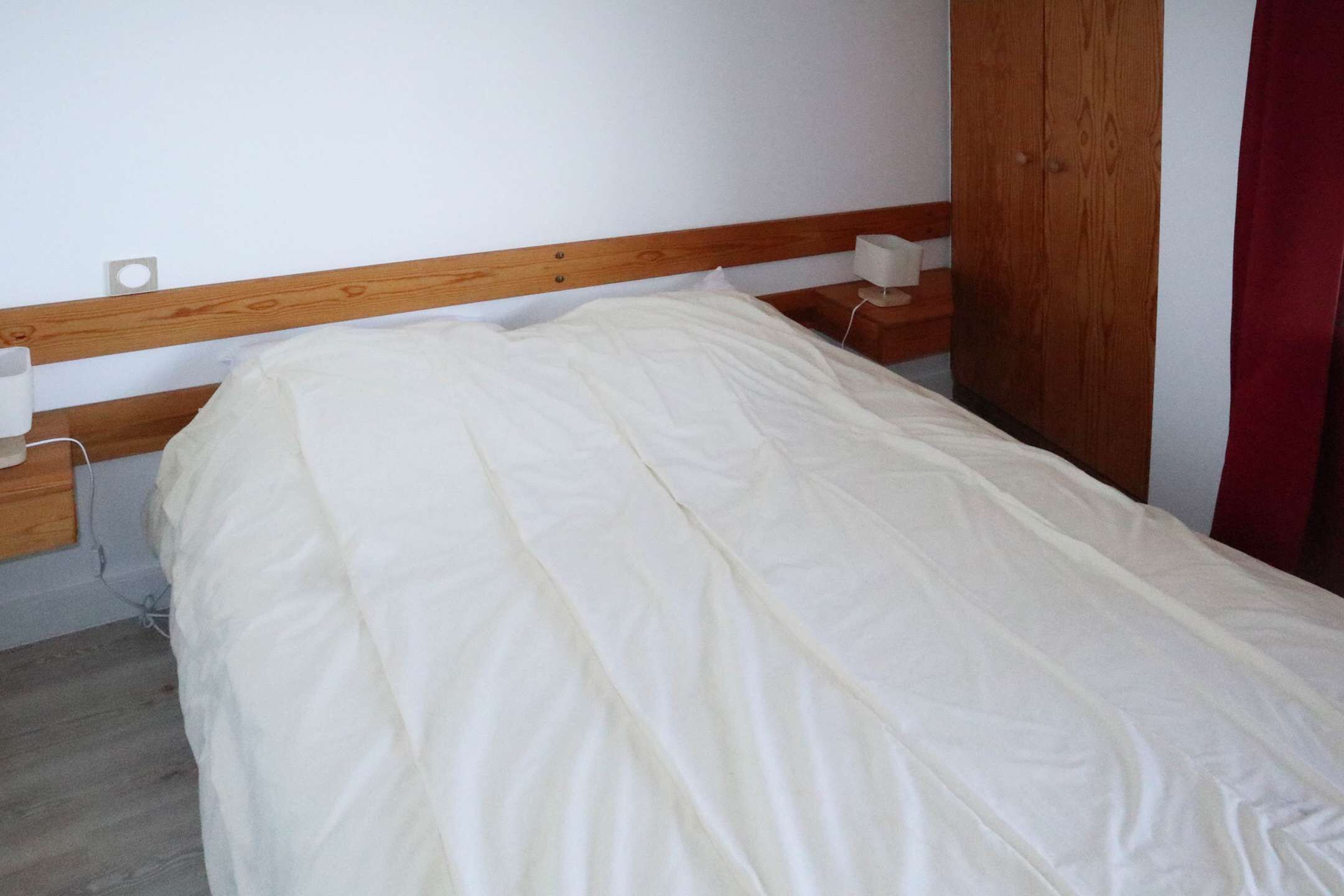 Una cama individual con cabecera de madera, una mesita de noche con lámpara y una cortina roja.