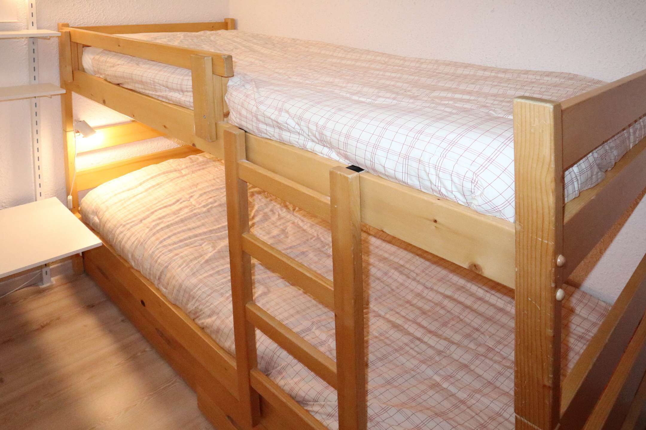 A bunk bed with a wooden frame and a mattress with a checkered pattern.